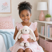 Bambina con coniglietto crema di peluche e abito rosa lavorato a maglia