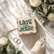 Boîte d’album photo en bois avec motif vert Love Like Jesus près d’alliances et de fleurs