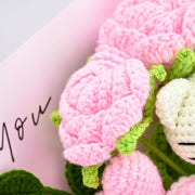 Makrodetail einer hellrosa Häkelrose mit grünen Kelchblättern neben dem weißen HK-Motiv
