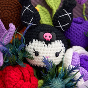 Macro view of black-and-white crochet KM doll with pink skull bow between red rose and purple tulip