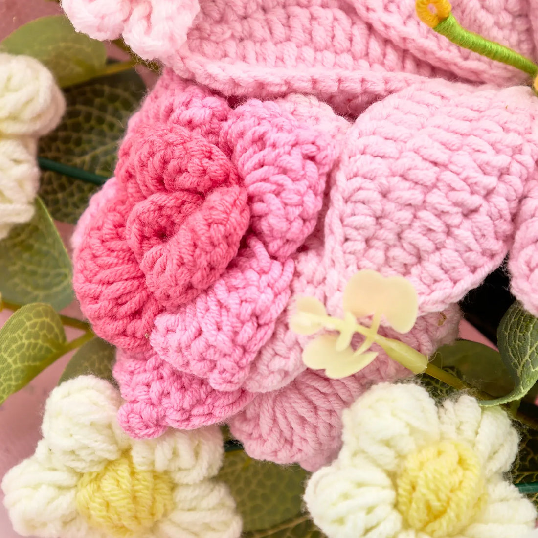 Macro detail of pink crochet rose beside lily petals and white puff flowers