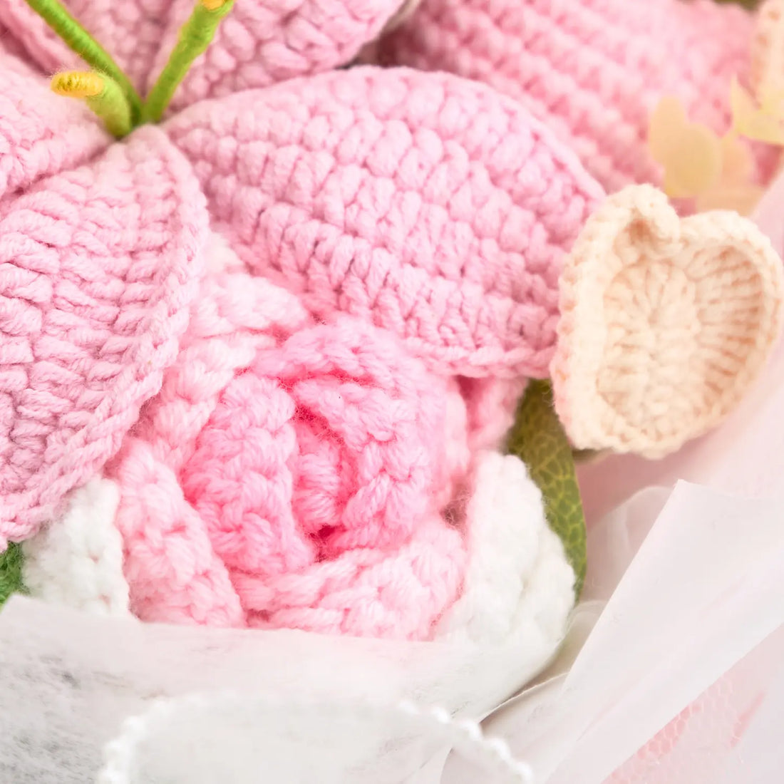 Macro view of pink crochet rose, lily petals, and cream heart accent