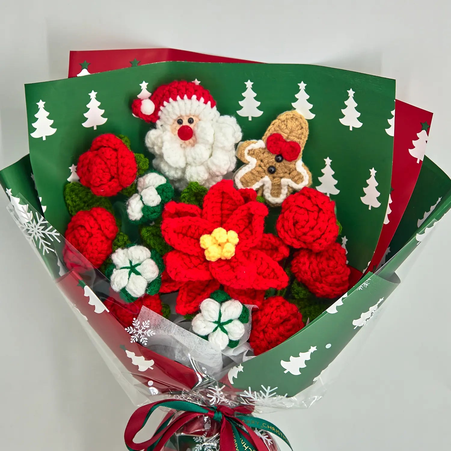 Vista ravvicinata del bouquet natalizio con stella di Natale rossa dal centro giallo, rose rosse e fiori di cotone bianchi nella carta verde con alberi