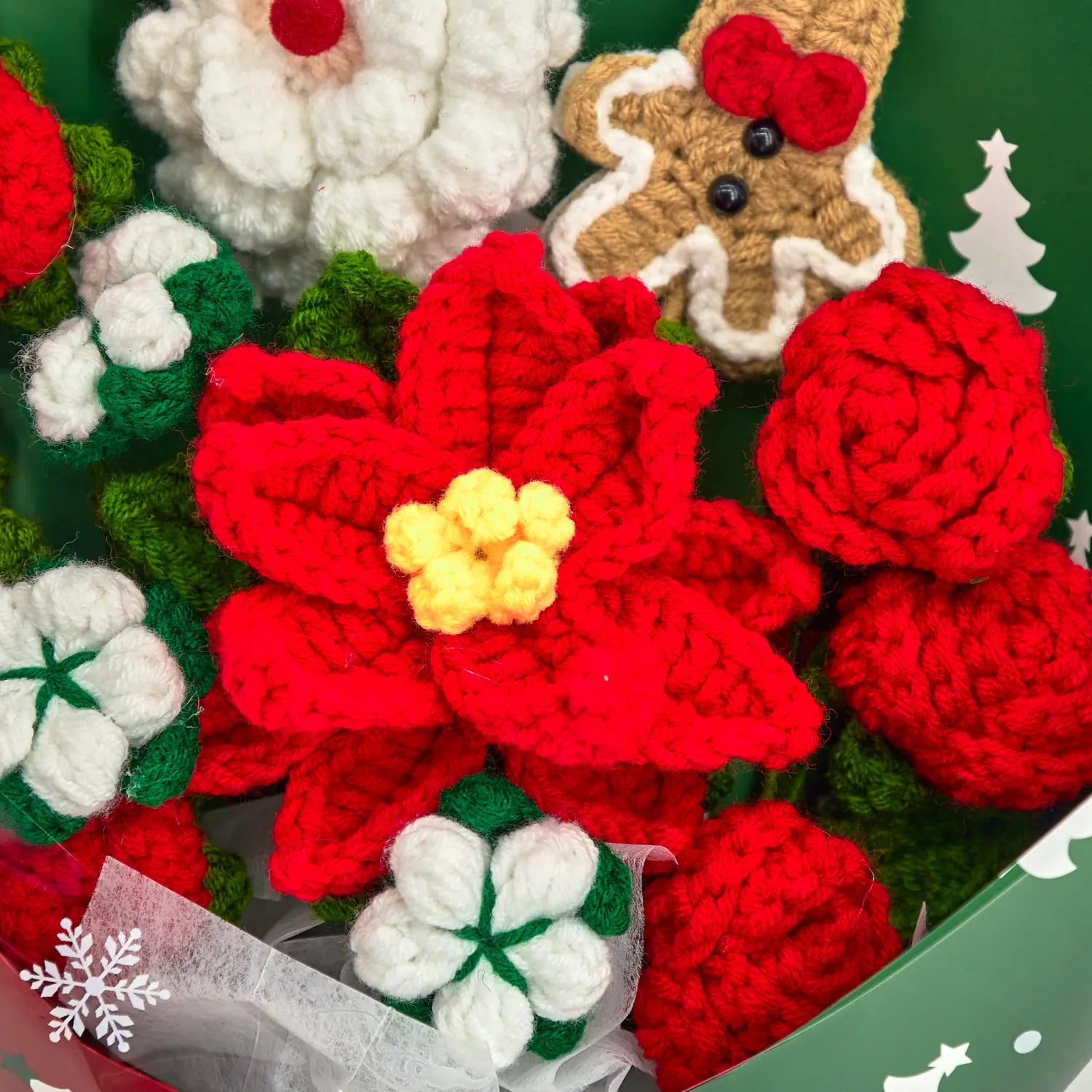 Dettaglio della stella di Natale rossa all’uncinetto con centro giallo, circondata da rose rosse e fiori di cotone bianchi