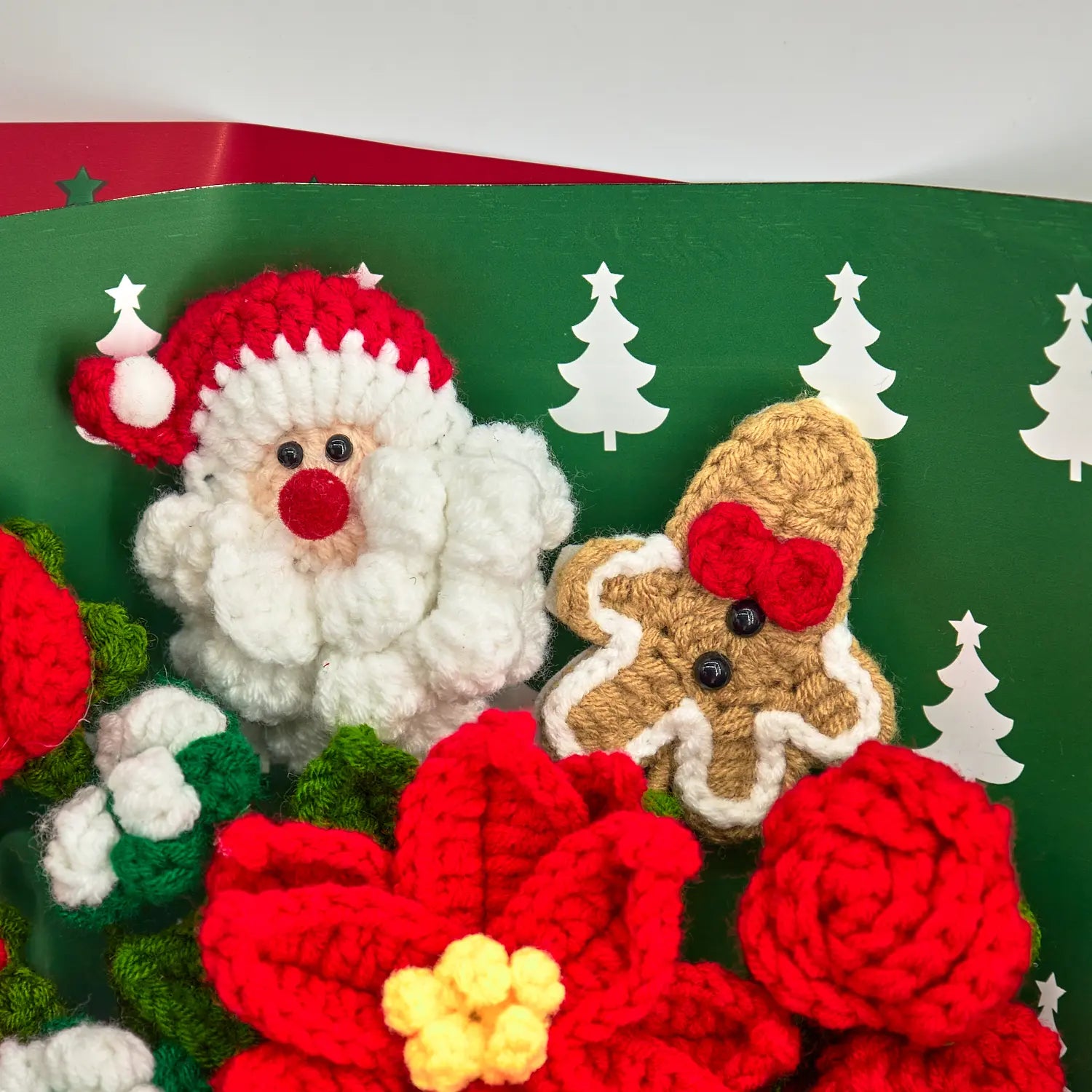 Primo piano di Babbo Natale all’uncinetto con cappello rosso accanto a un omino di pan di zenzero con fiocco rosso