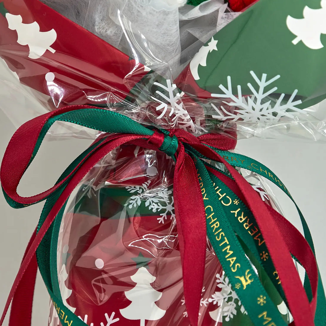 Dettaglio dei nastri rossi e verdi annodati intorno alla confezione natalizia con fiocchi di neve e alberi bianchi e la scritta Merry Christmas