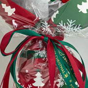 Dettaglio dei nastri rossi e verdi annodati intorno alla confezione natalizia con fiocchi di neve e alberi bianchi e la scritta Merry Christmas