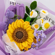 Close-up of purple crochet bouquet with large sunflower, purple rose, tulip, lavender, white flowers, and green leaves
