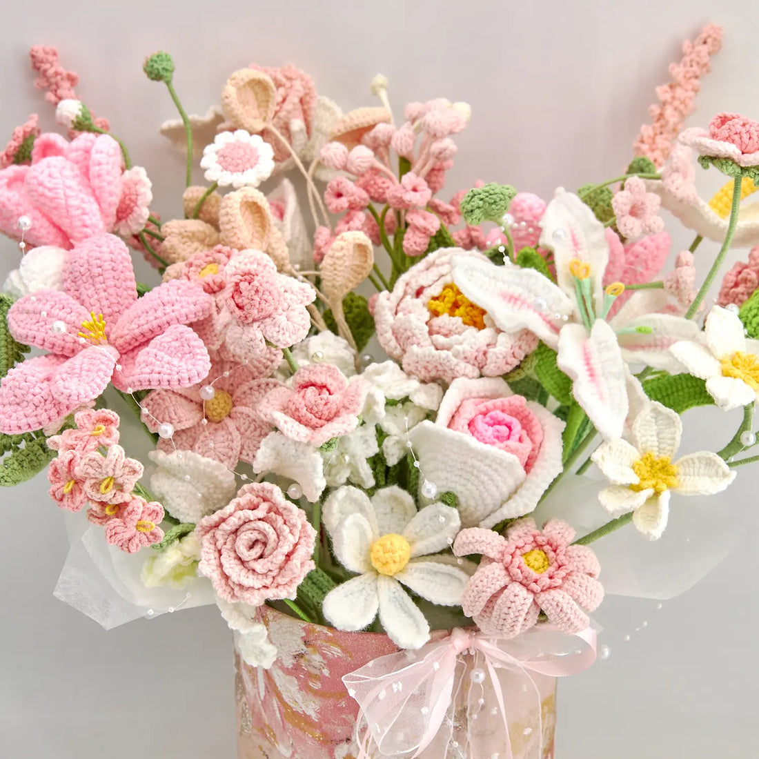 Close view of pink and white crochet flowers with rose-, lily-, and daisy-shaped blooms in a pink gift box
