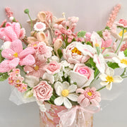 Close view of pink and white crochet flowers with rose-, lily-, and daisy-shaped blooms in a pink gift box