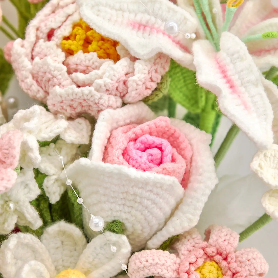 Close-up of a pink crochet rose-shaped bloom beside a pale pink layered flower and white lily-shaped petals