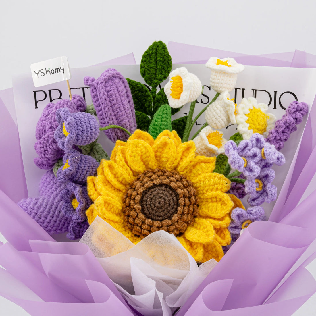 Front view of purple crochet bouquet with oversized sunflower, purple rose, white lily-of-the-valley flowers, and lavender