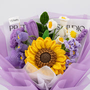 Front view of purple crochet bouquet with oversized sunflower, purple rose, white lily-of-the-valley flowers, and lavender