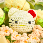 淡い黄色のバラとピーチ色の花に囲まれた、赤いリボン付きの白いかぎ針編みHKキャラクターの顔の接写
