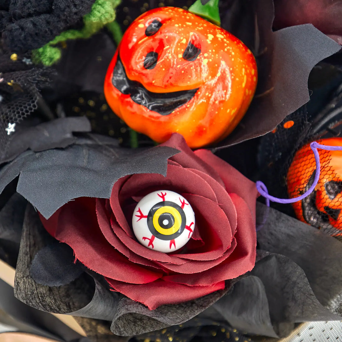 Dettaglio macro di una zucca arancione e di un ornamento a forma di occhio inserito in un fiore rosso scuro