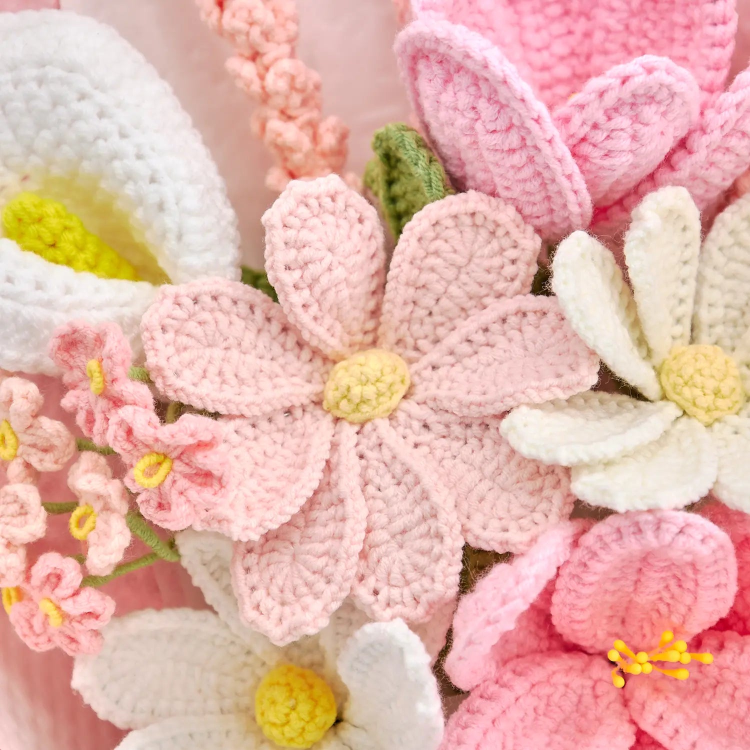 Dettaglio di fiori aperti all’uncinetto rosa chiaro e bianchi accanto a un fiore bianco a forma di calla