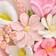 Dettaglio di fiori aperti all’uncinetto rosa chiaro e bianchi accanto a un fiore bianco a forma di calla
