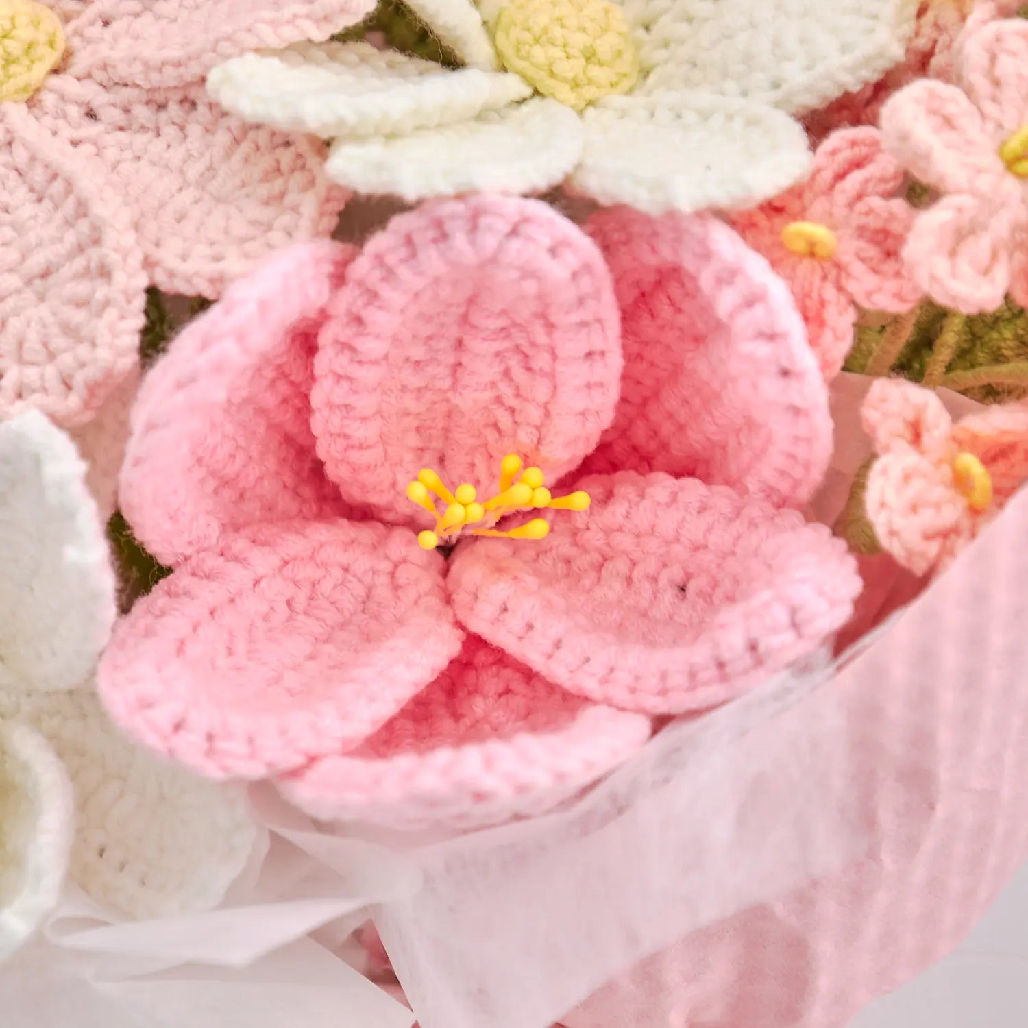 Primo piano di un fiore all’uncinetto rosa intenso con stami gialli nel bouquet incartato