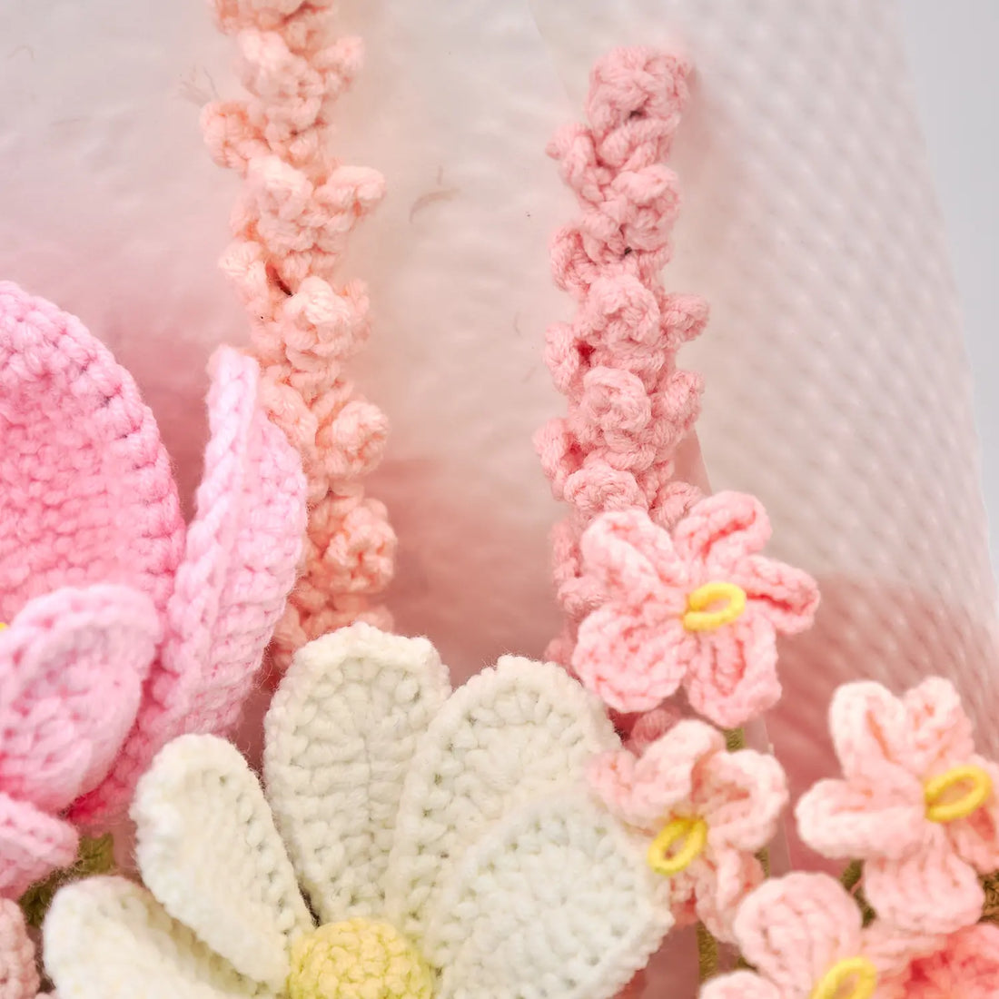 Primo piano di steli rosa all’uncinetto tipo lavanda, piccoli fiori e un fiore bianco aperto