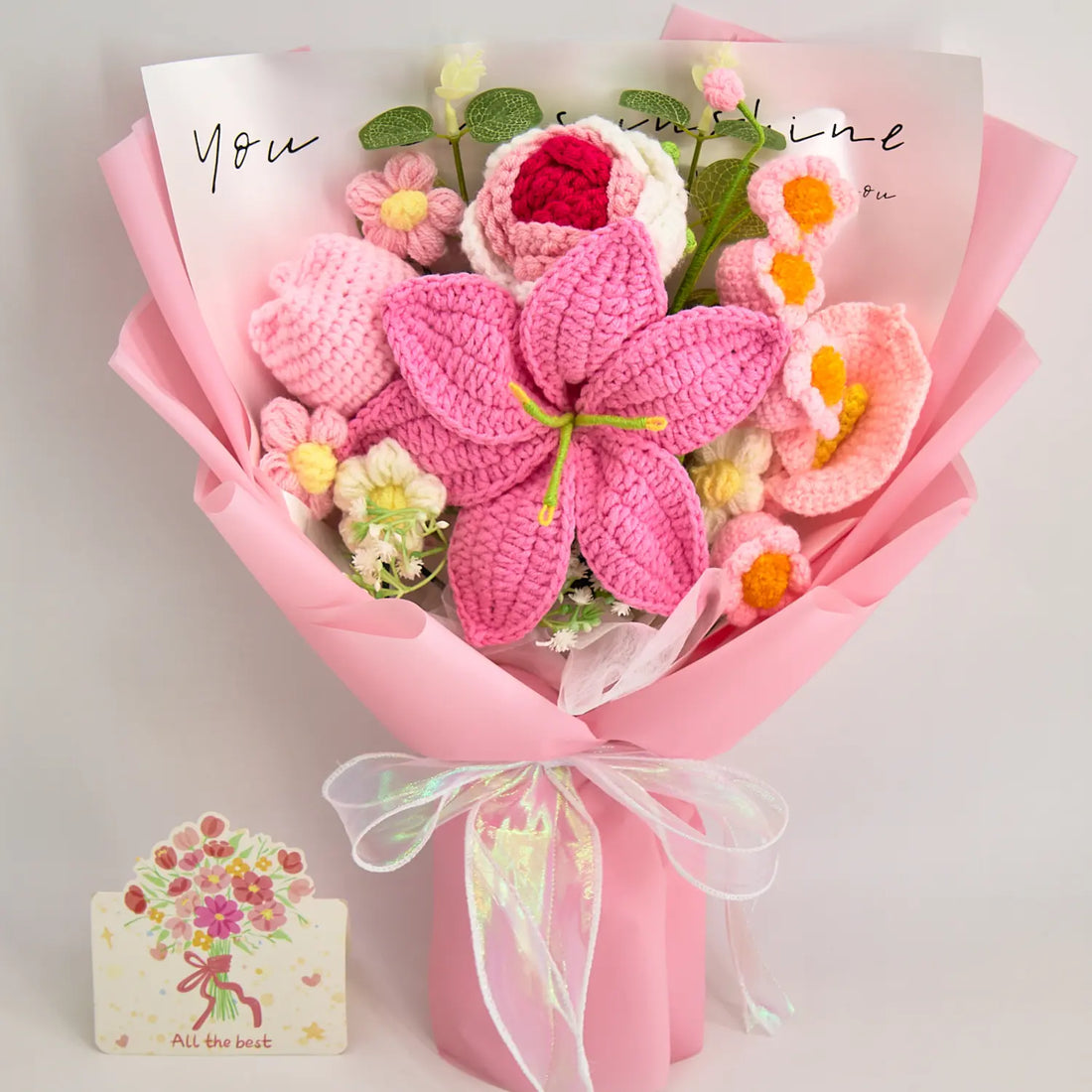 Vorderansicht eines rosa Häkelblumenstraußes mit großer Lilie, Rose, Tulpe und Calla in rosa Papier mit einer durchscheinenden Schleife