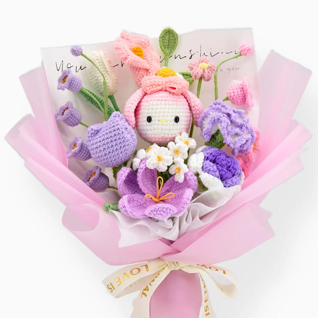 MLうさぎドール、重なる花、クリーム色のリボン、ピンクのラッピングを正面から見たピンクとパープルのかぎ針編みブーケ