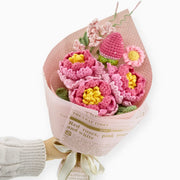 Crochet peony bouquet with strawberries and daisies in newspaper-style wrapping