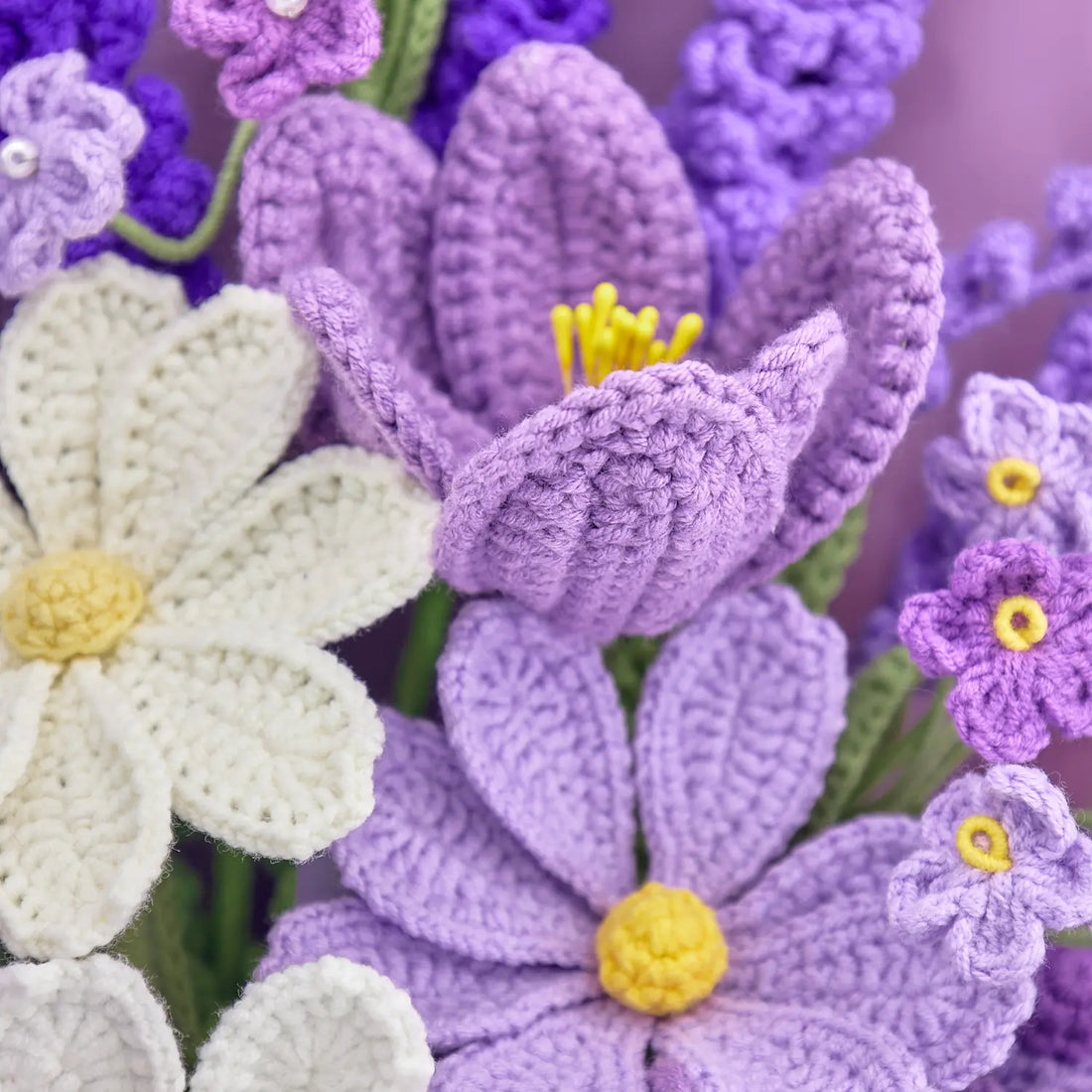 Primo piano di fiori viola all’uncinetto a forma di giglio accanto a un fiore bianco stile Galsang e piccoli fiori viola con centro giallo