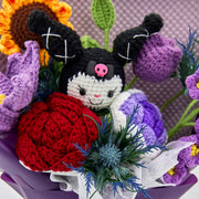 Close-up of crochet KM doll between red rose, purple tulip, sunflower, and blue artificial greenery