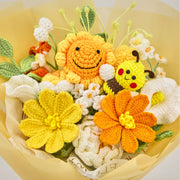 Primer plano de girasol sonriente y abeja de ganchillo entre flores amarillas, naranjas y blancas con hojas verdes
