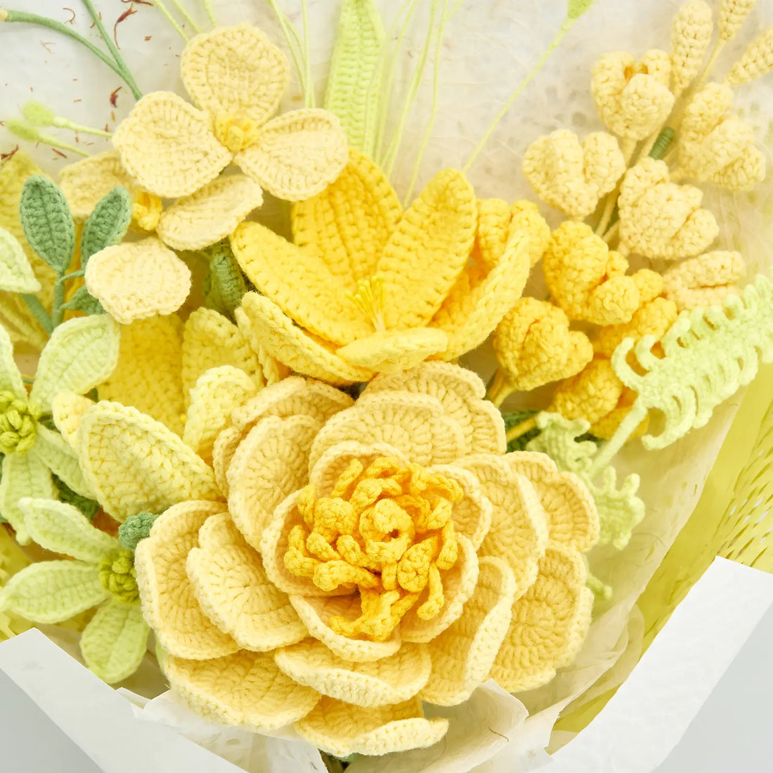 Close-up of large layered light-yellow crochet bloom beneath yellow lily-shaped flower and smaller cream flowers