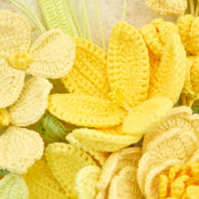 Close-up of open yellow lily-shaped crochet flower among cream petals and pale green leaves